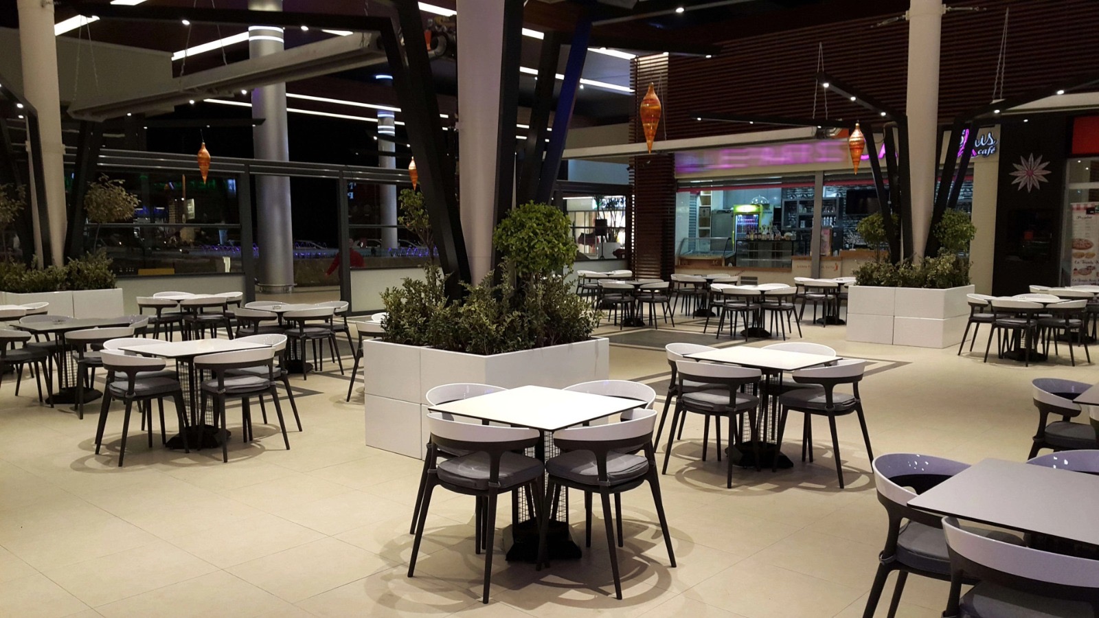 Kafe alanında beyaz kare masa tablaları ve koyu sandalyeler